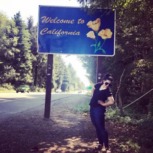 Janna Haider next to Welcome to California sign next to a road