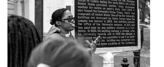 Women in front of a The Little Round House sign with caption "Author discussing the Little Round House marker on a February 2020 Hallowed Grounds tour. (Photo by author)"