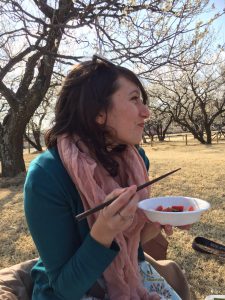 Mika Thornburg eating fruit with chopsticks with field and trees behind her
