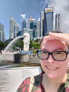 Kristen smiling in front of the Singapore skyline and Merlion statue.