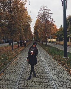 Chloe Roberts standing on cobblestone and tracks surrounded by fall trees in Prague